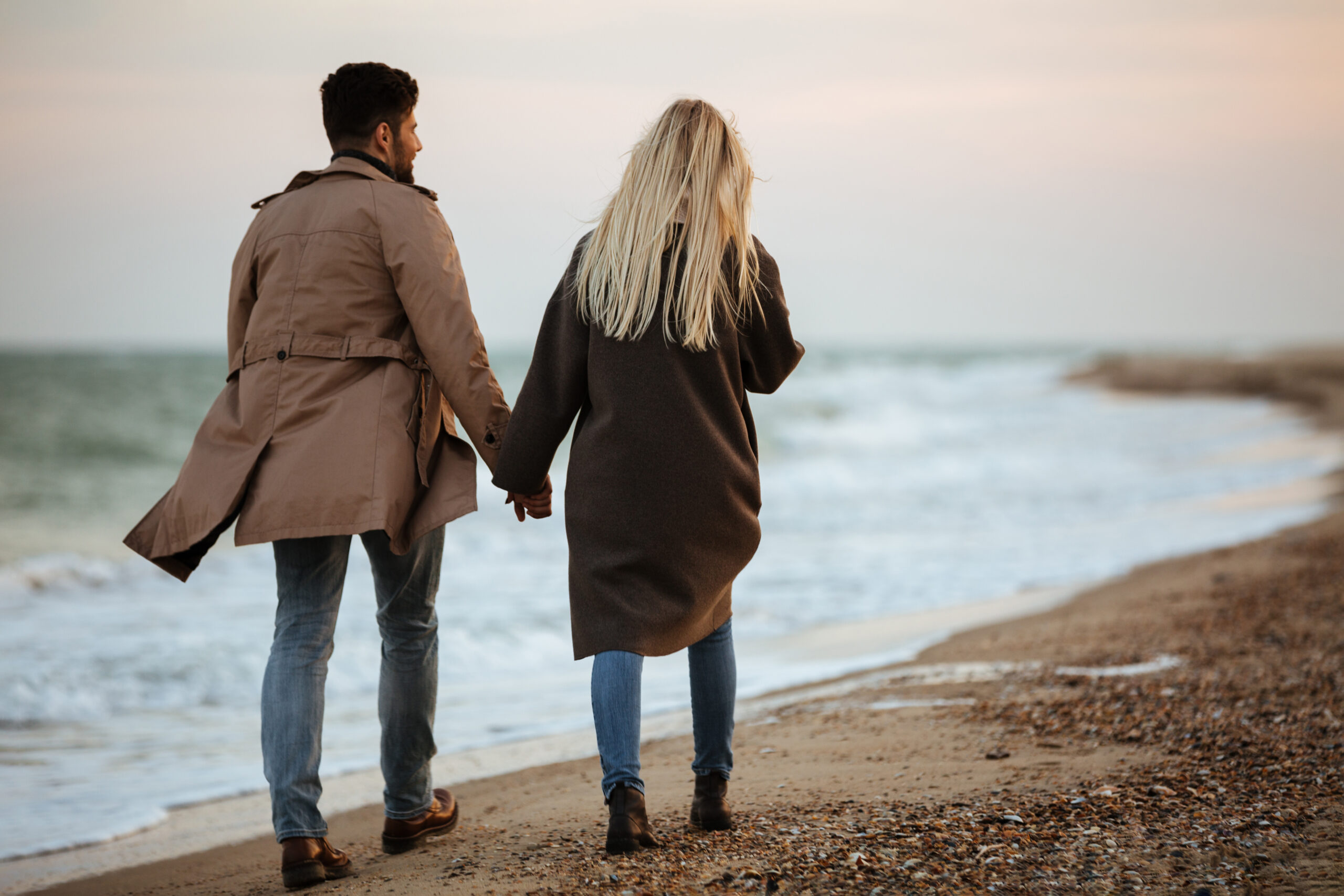 Paar hält Händchen bei einem Spaziergang am Strand – Symbol für Liebe, Beziehungen und die Theorie der drei großen Lieben.
