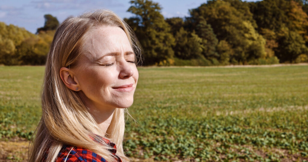 Frau in der Natur, die innehält, um auf ihre innere Stimme zu hören und neue Kraft zu finden.